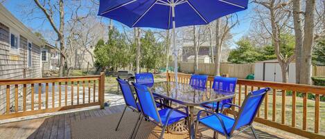 A deck with a table and chairs, a blue umbrella, and a wooden railing.