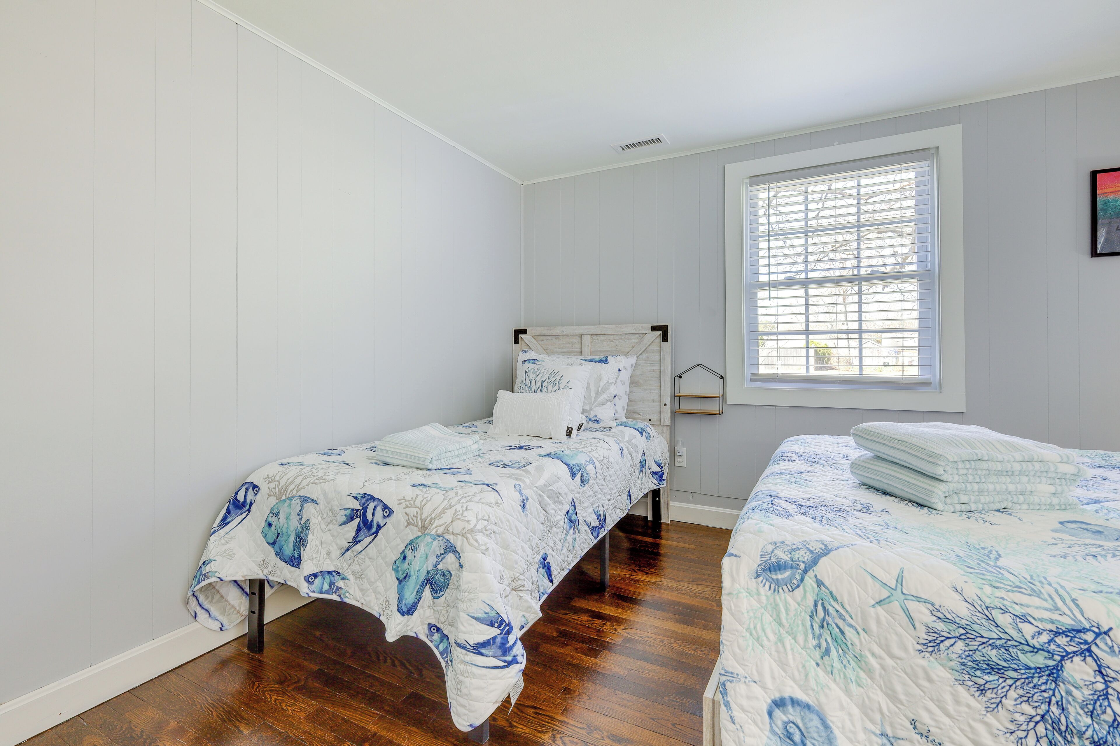 A bedroom with two single beds, a window with blinds, and a white wall.