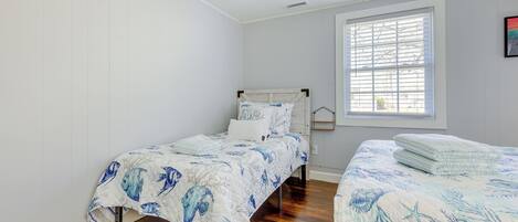 A bedroom with two single beds, a window with blinds, and a white wall.