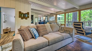 Un salón acogedor con un sofá color beige, suelo de madera y ventanas amplias con vistas al exterior.