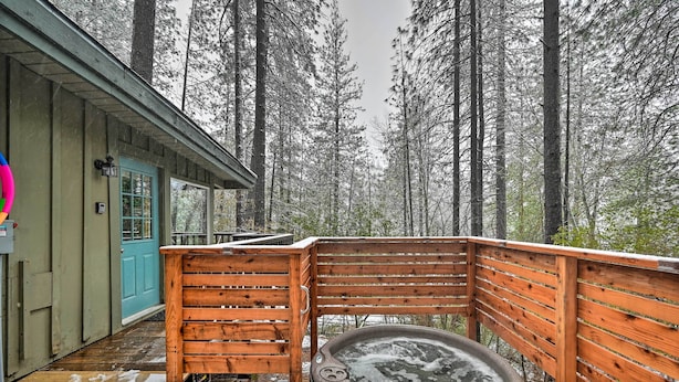 Una terraza de madera con un jacuzzi, una puerta azul y vistas a altos árboles.