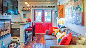 A cozy living room with a red door, a sofa with colorful cushions, a television, and a painting on the wall. - Walkable Studio Apartment in Downtown Livingston! (Livingston)