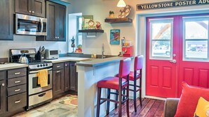 A kitchen with dark cabinets, stainless steel appliances, a red door, and a bar area. - Walkable Studio Apartment in Downtown Livingston! (Livingston)