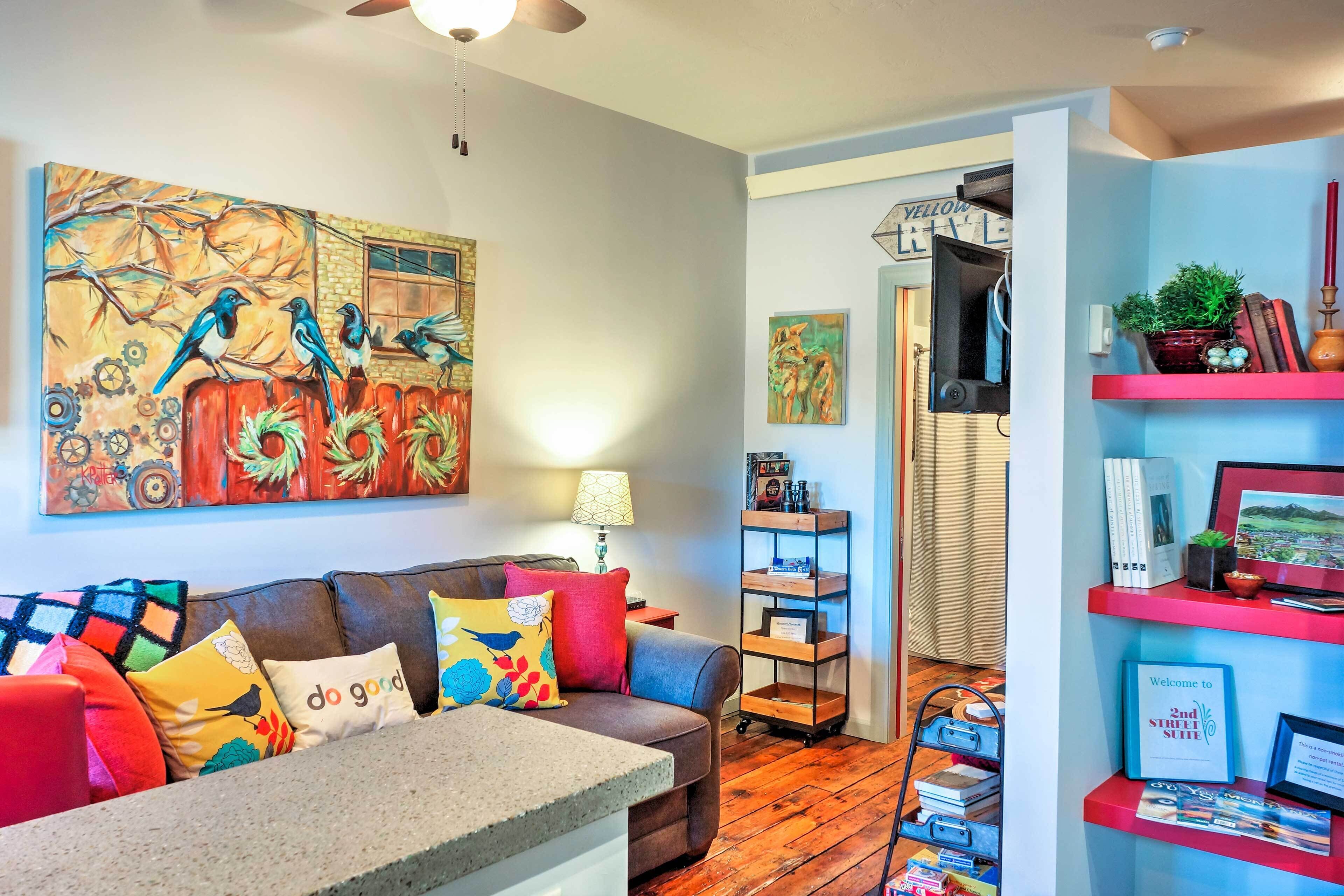 A cozy living room with a brown leather sofa, colorful cushions, a large abstract painting, and a wooden floor.