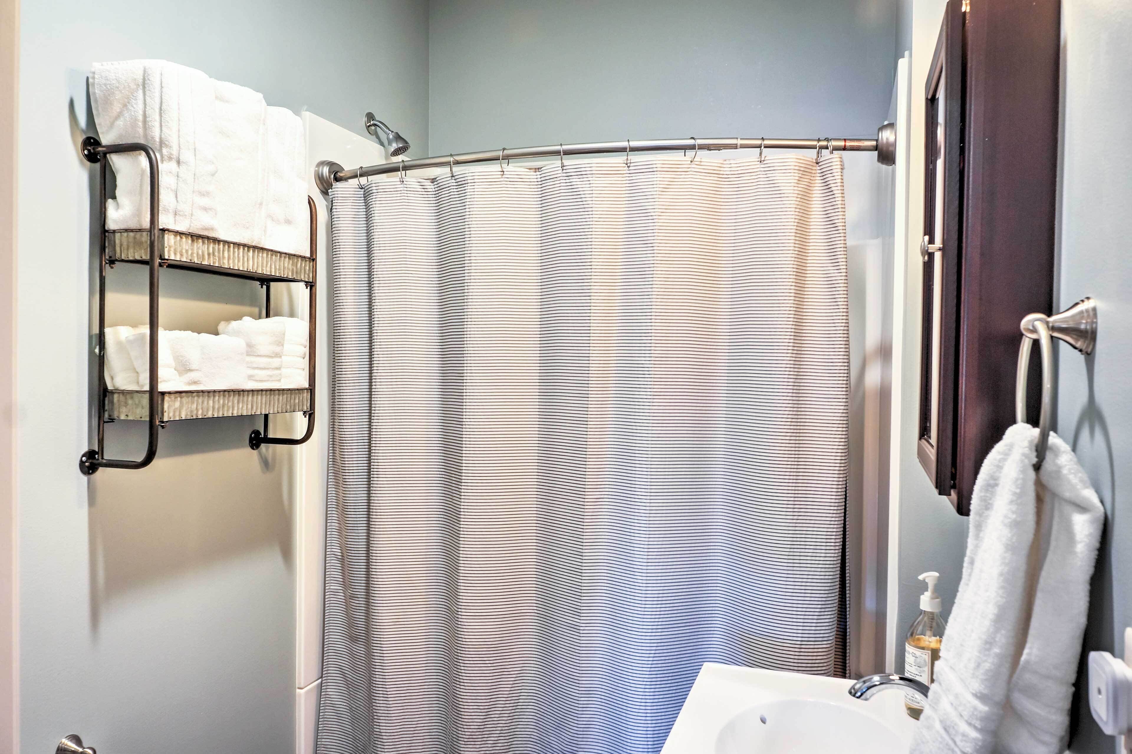 Ein Badezimmer mit Duschvorhang, Handtuchhalter mit Handtüchern und Waschbecken mit Seifenspender.