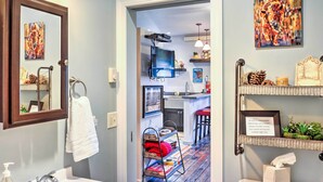 A modern bathroom with a sink, mirror, and towel rack. A hallway leads to a kitchen area with a TV and bar stools. - Walkable Studio Apartment in Downtown Livingston! (Livingston)