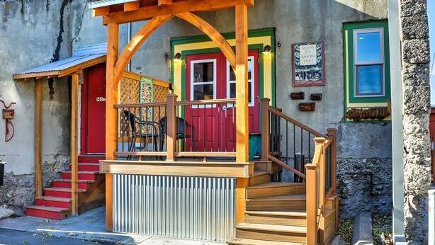 A colorful building with a wooden porch, a red door, and a staircase leading to a green door. - Walkable Studio Apartment in Downtown Livingston! (Livingston)