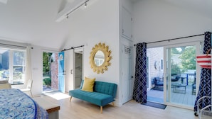 Een moderne slaapkamer met een bed, een bank, een grote spiegel en een glazen schuifdeur naar een terras.