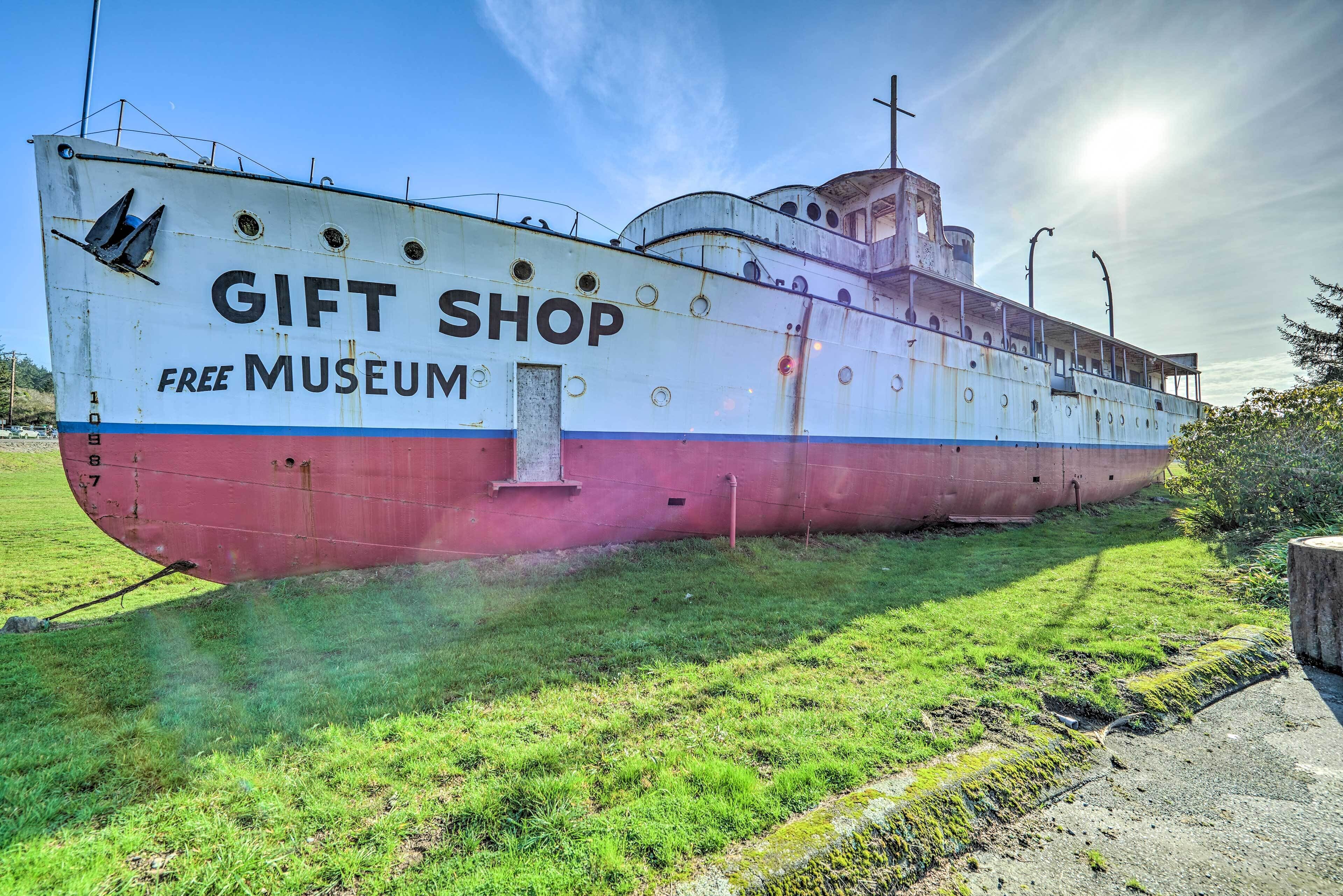 Um navio grande e imóvel com a inscrição 'GIFT SHOP FREE MUSEUM' na lateral, estacionado em uma área gramada.
