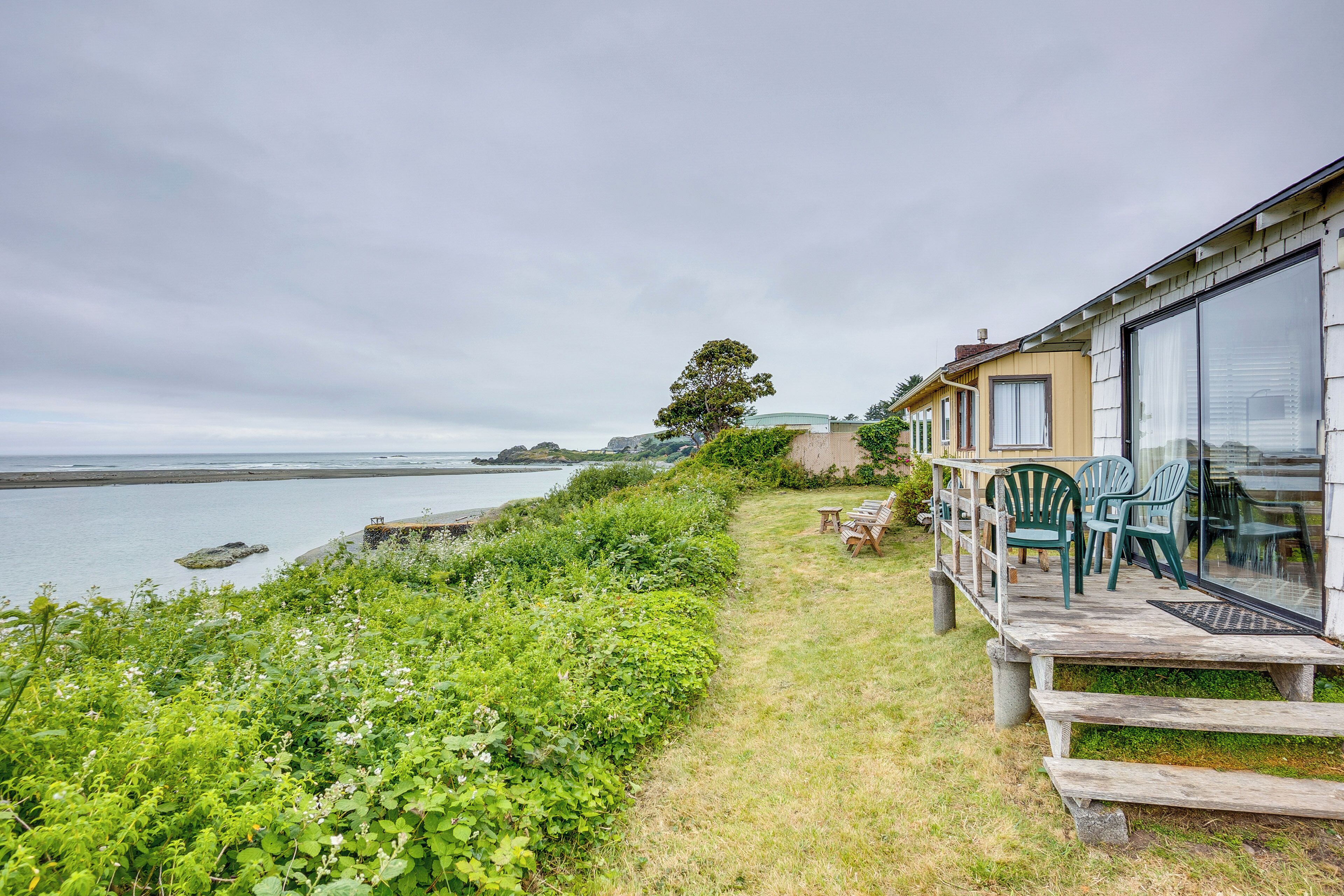 Une propriété située en bord de mer, dotée d’une terrasse en bois, d’un espace salon extérieur et offrant une vue sur la mer.