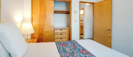 Un dormitorio con cama, mesita de noche, lámpara, armario de madera y baño visible a través de una puerta abierta.