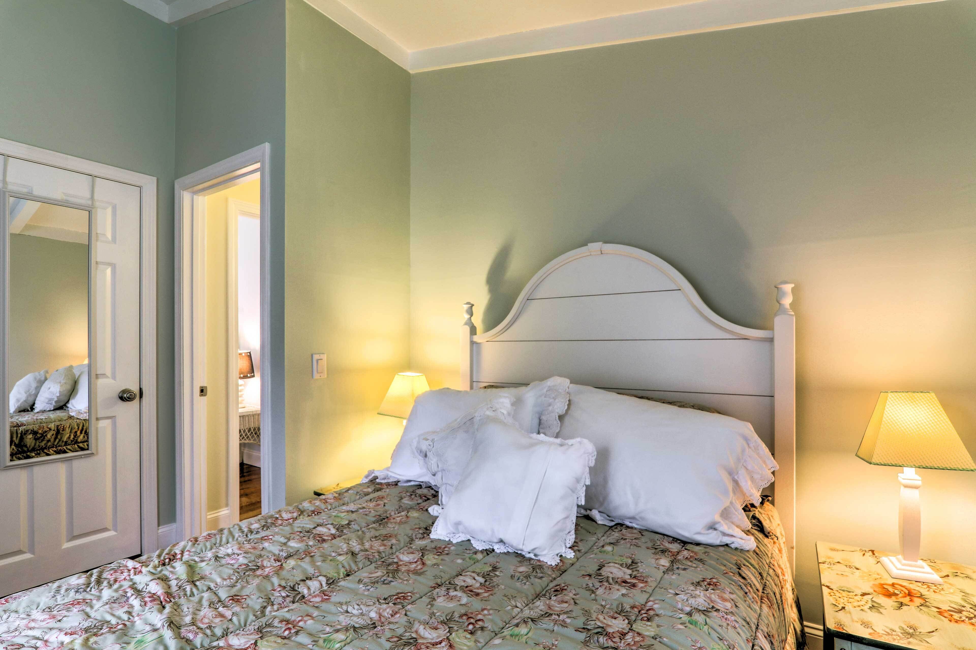 Een netjes opgemaakt bed met bloemenbedrukking, een wit hoofdeinde en twee bedlampjes.