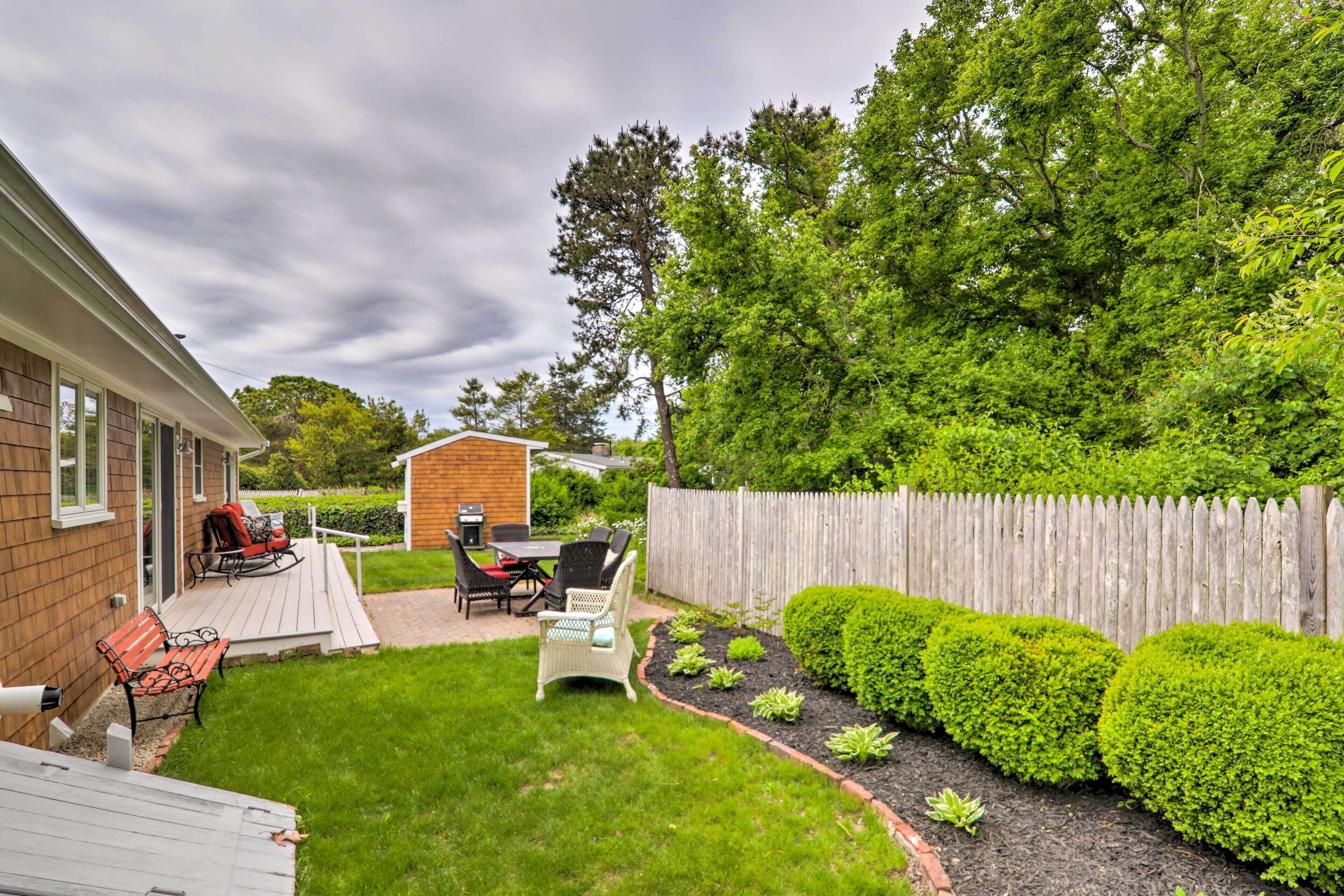 Ein Garten mit Holzterrasse, Grillplatz und umzäunter Garten mit ordentlich geschnittenen Büschen.