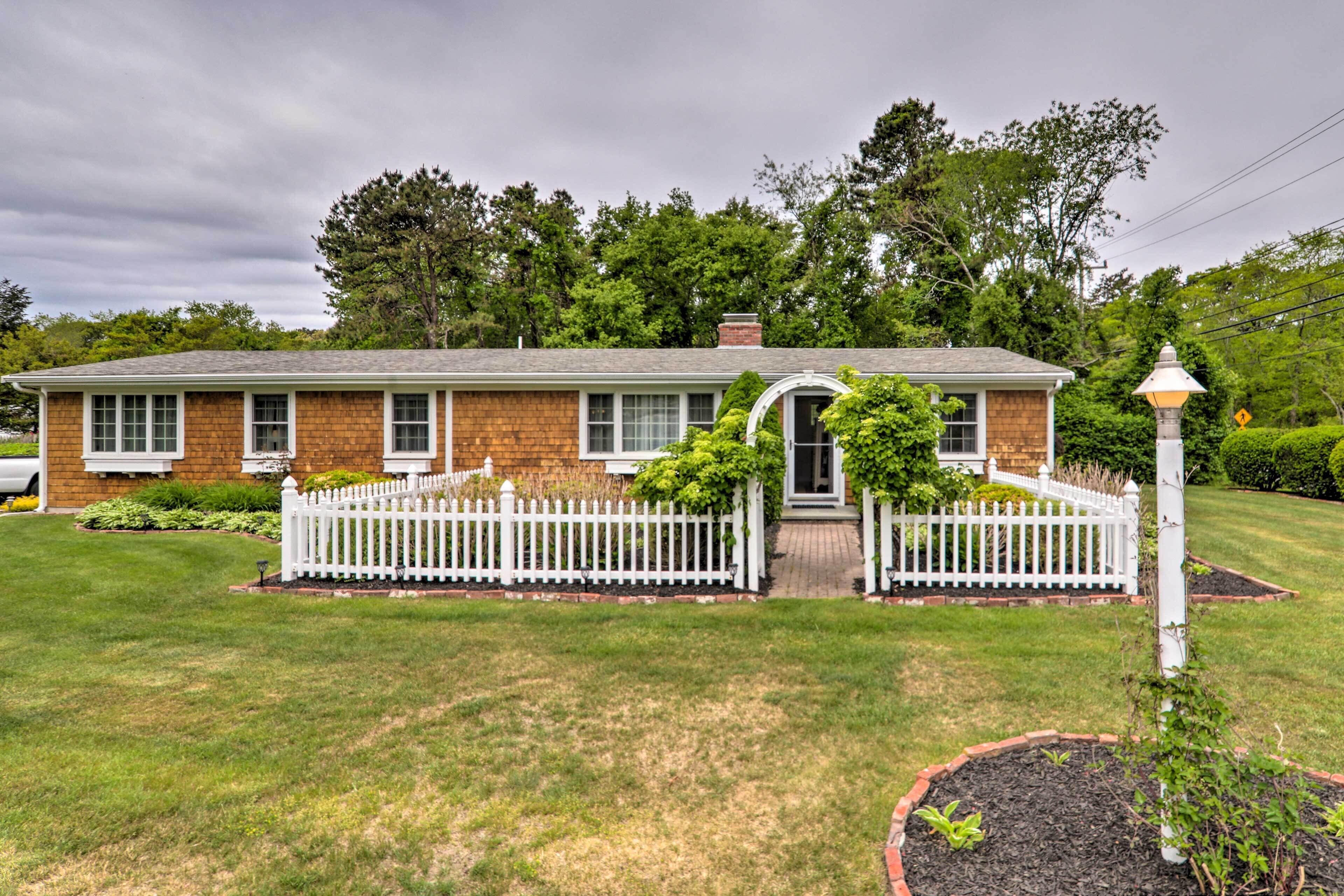 A two-story brick house with a white picket fence, a front porch, and a small garden area.