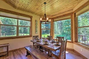 A wooden dining room with a large table set for six, large windows, and a 'Gather Here' sign on the wall. - Bigfork Modern Living - Pet & Family Friendly! (Bigfork)