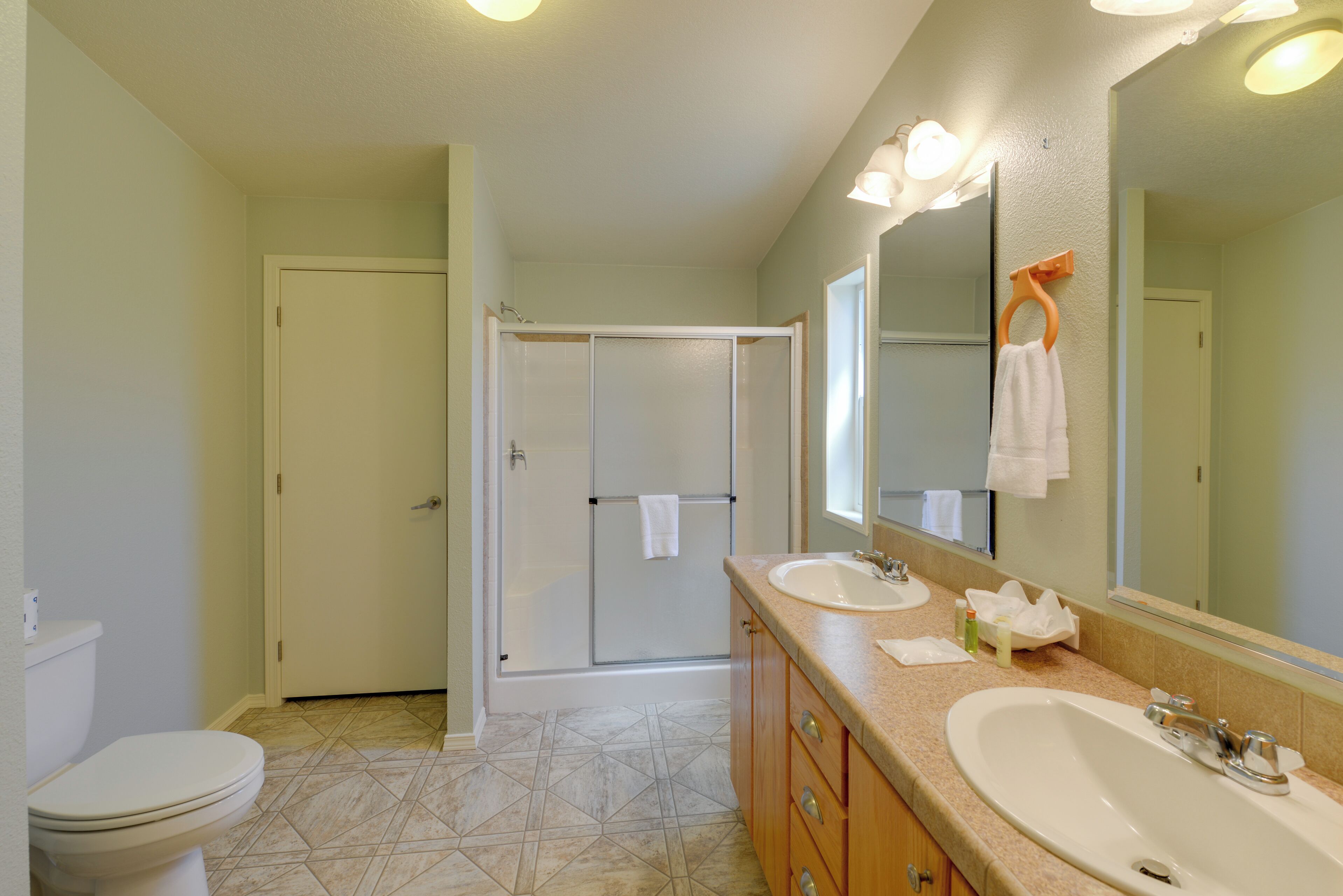 Une salle de bain avec des toilettes, deux lavabos, une douche et un grand miroir.