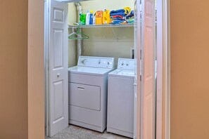 A laundry room with two white washing machines and a shelf above holding cleaning supplies and folded clothes. - Family-friendly Hancock Home: Walk to Slopes! (Hancock)