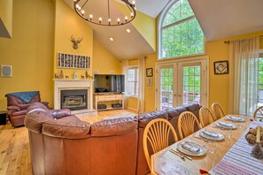 A cozy living room with a fireplace, a large window, and a dining area set for six. - Family-friendly Hancock Home: Walk to Slopes! (Hancock)