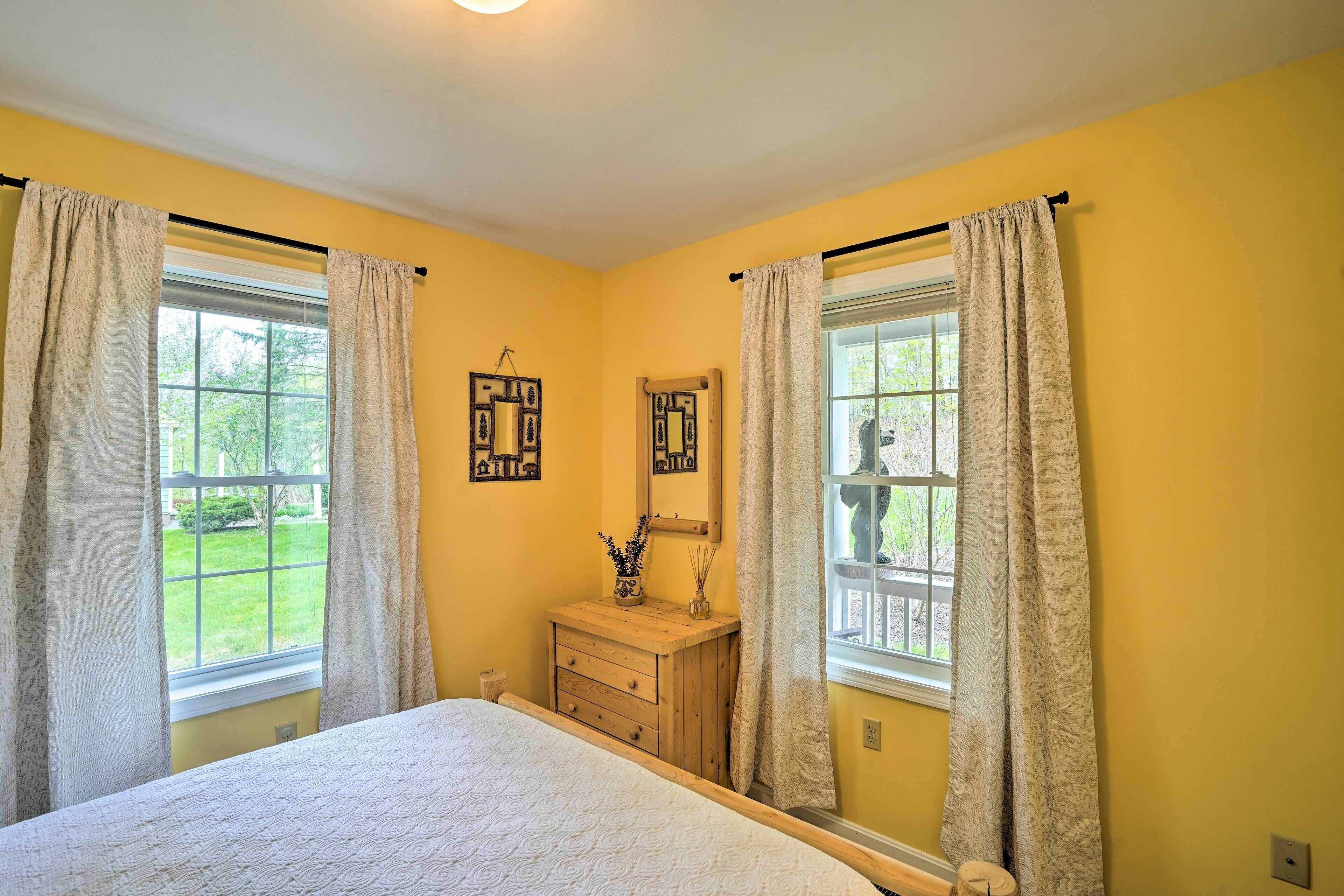 A bedroom with a bed, two windows with curtains, a dresser, and wall decorations.