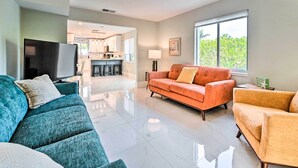 Ein modernes Wohnzimmer mit einem türkisblauen Sofa, einem orangefarbenen Sofa und einem gelben Sessel. Ein Flachbildfernseher ist an der Wand befestigt.