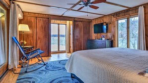 A bedroom with a large bed, a ceiling fan, a TV mounted on the wall, and a view of the outdoors through a sliding door.
