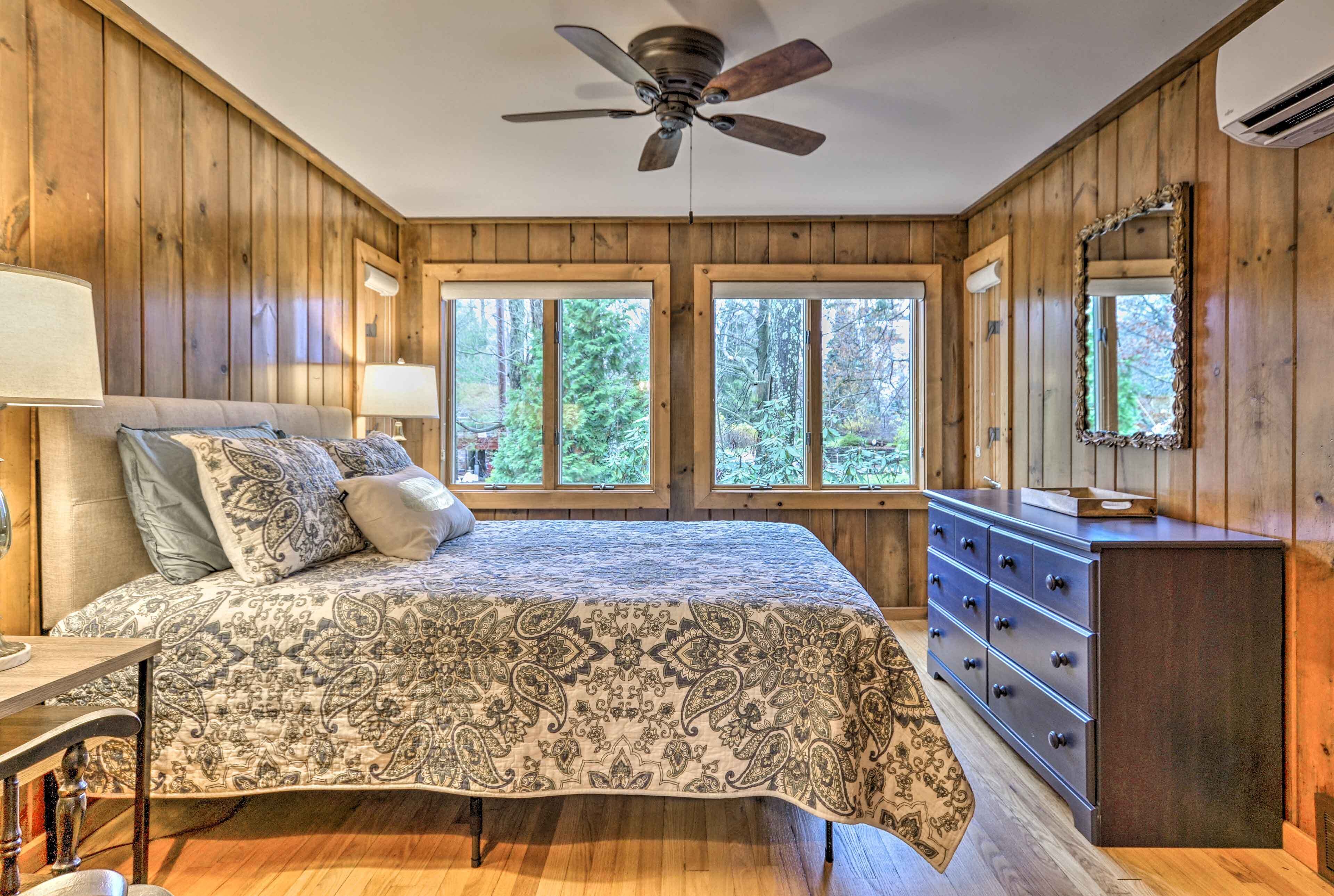 A bedroom with a bed, dresser, and windows with a view of trees.