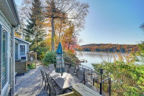 Une terrasse avec des sièges extérieurs et une vue sur un lac entouré d’un paysage automnal.
