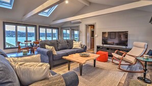 A spacious living room with a large TV, comfortable seating, and a view of the water.