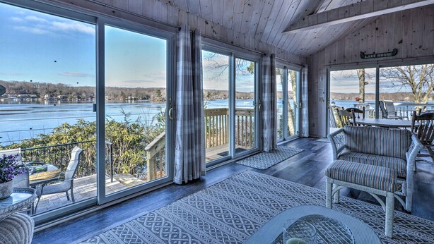 A spacious porch with large windows offering views of a lake and surrounding landscape.