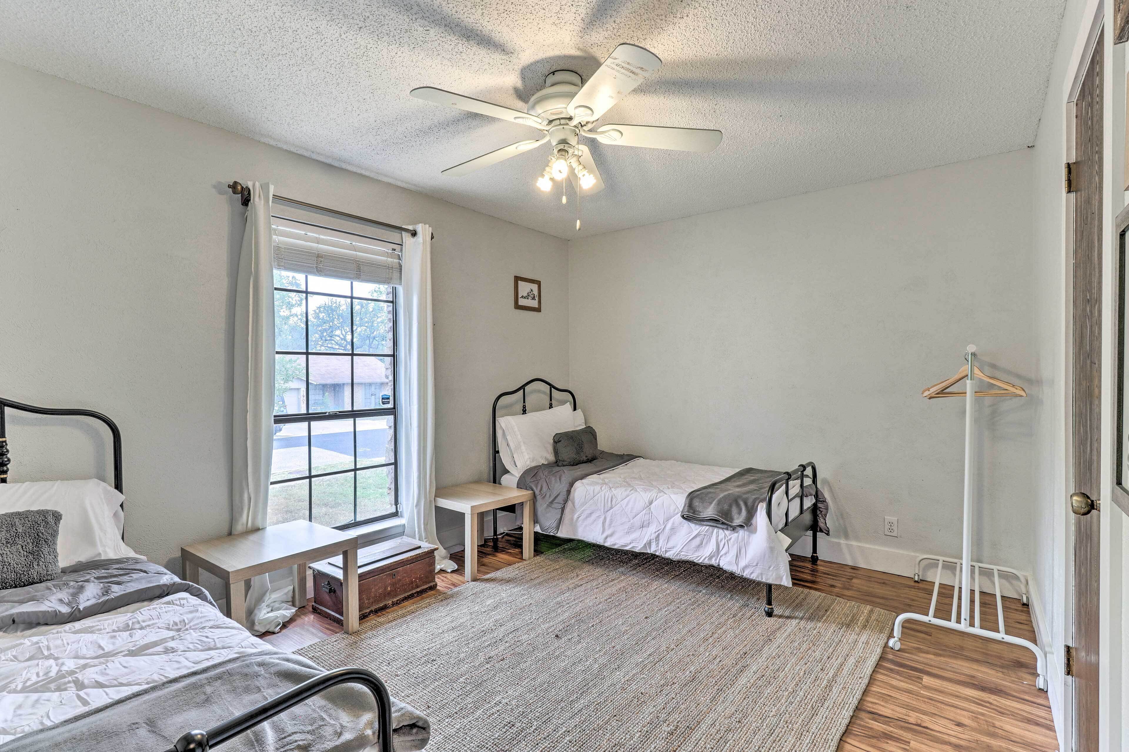 A bedroom with two beds, a ceiling fan, a window, a bedside table, and a coat rack.