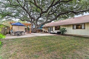 A backyard with a covered patio, a lawn, and a house with a porch. - Pet-friendly Austin Ranch Home w/ Fire Pit! (Austin)