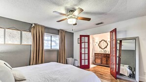 A bedroom with a bed, a ceiling fan, a window with curtains, a red door, a mirror, and a dresser. - Pet-friendly Austin Ranch Home w/ Fire Pit! (Austin)
