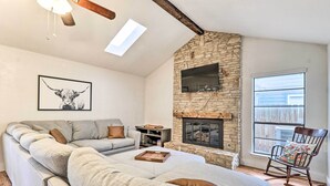 A cozy living room with a stone fireplace, a large sofa, a rocking chair, and a TV mounted on the wall. - Pet-friendly Austin Ranch Home w/ Fire Pit! (Austin)