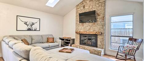 A cozy living room with a stone fireplace, a large sofa, a rocking chair, and a TV mounted on the wall.