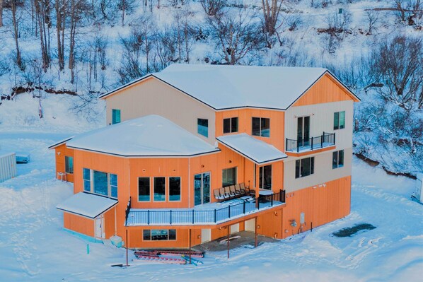 Une maison à plusieurs étages, dont le toit est recouvert de neige, et qui possède un balcon avec des sièges pour l’extérieur.