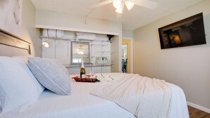 A bedroom with a bed, a ceiling fan, a wall-mounted TV, and a mirror.