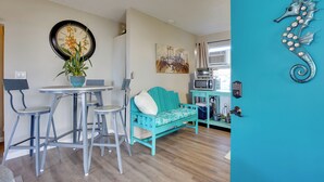 A room with a teal sofa, a dining table with chairs, a clock, and a seahorse decoration.