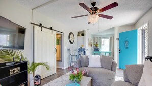 A living room with a ceiling fan, a TV, a bookshelf, a coffee table with a book, and a sofa.