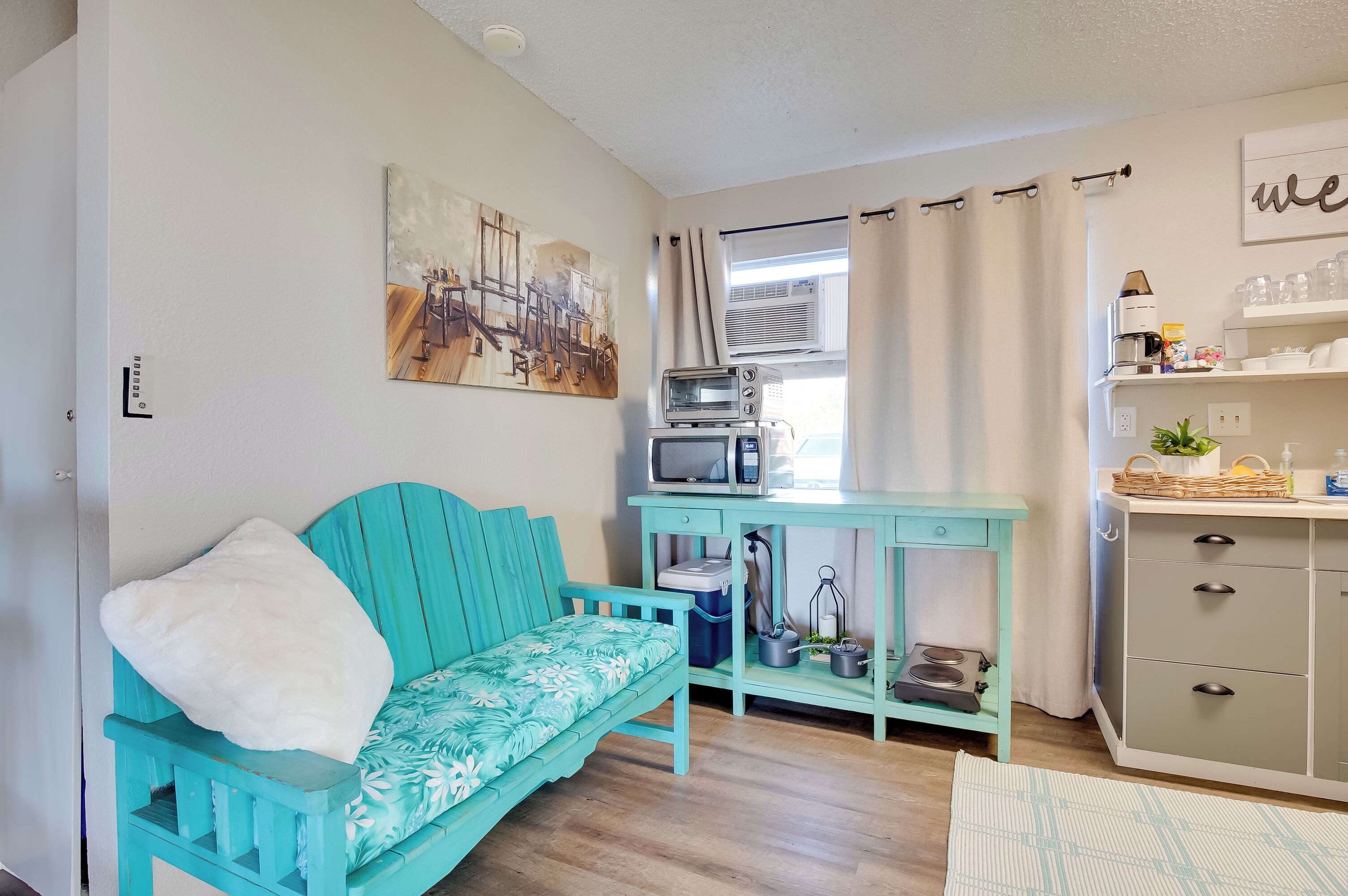 A compact living space with a teal sofa, a small kitchenette, and a painting on the wall.