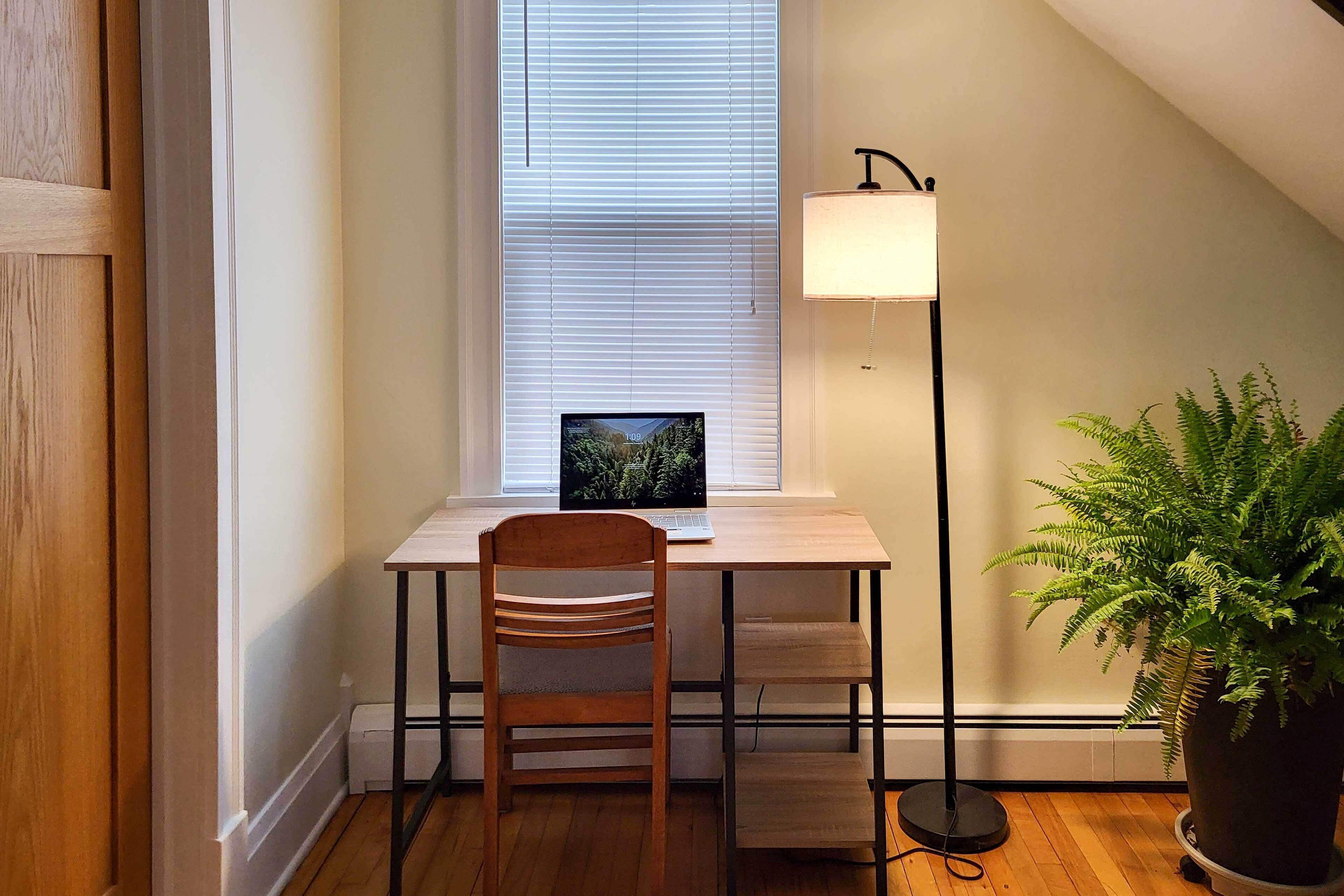 Quarto com escrivaninha, cadeira, laptop e planta em vaso.