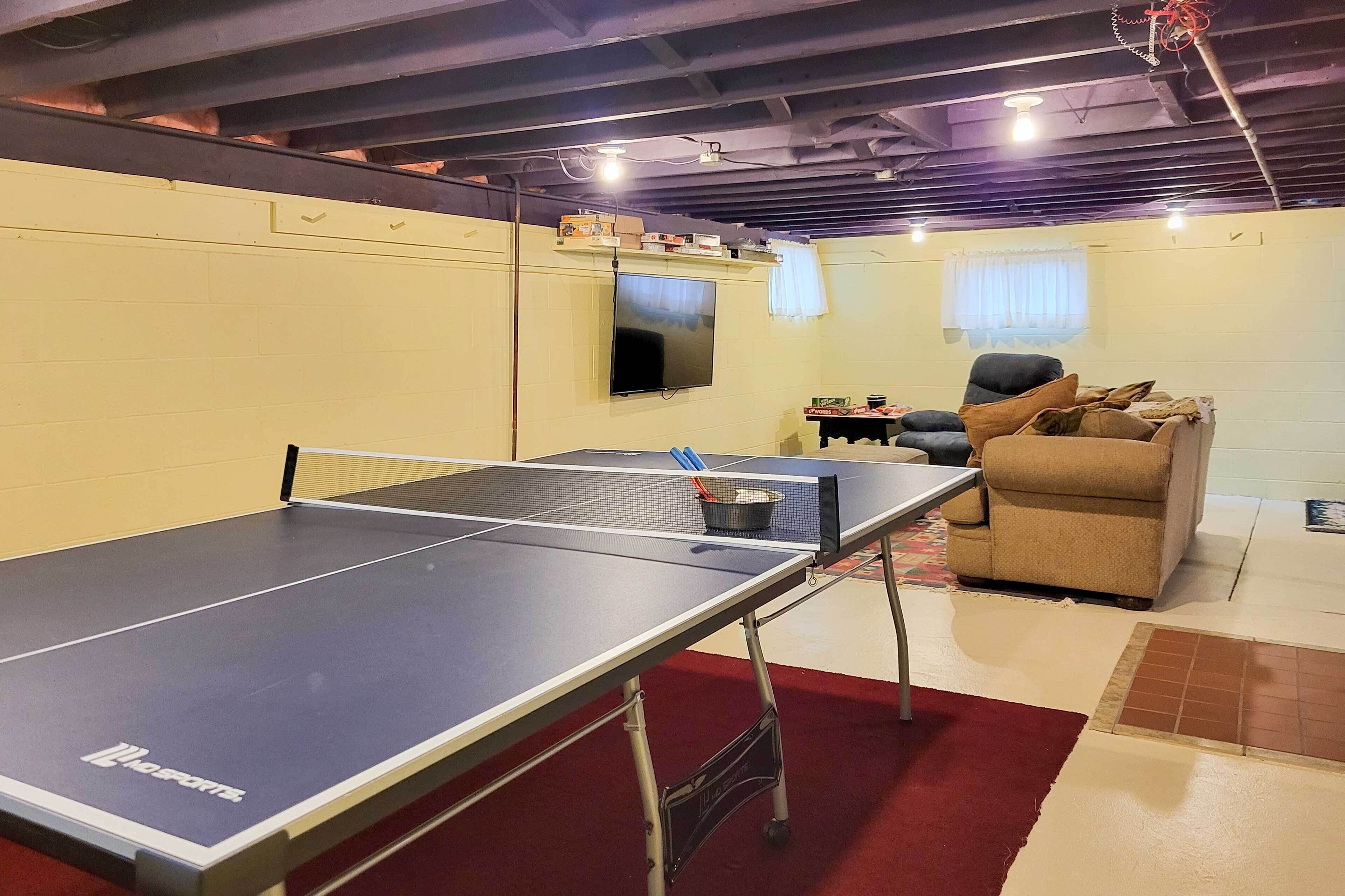 A ping pong table in a room with a TV, a couch, and a small table with items on it.