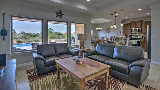 A spacious living room with leather sofas, a wooden coffee table, and large windows offering a view of the outdoors. - South Padre Paradise w/ Saltwater Pool Near Golf! (Port Isabel)