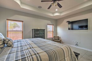 Un dormitorio con cama, ventilador de techo, cómoda, una silla y televisor instalado en la pared.