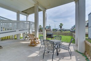 A covered patio with a table and chairs, a grill, and a wooden rocking chair. - Furnished Deck + Ocean Views: Surfside Beach Home (Freeport)