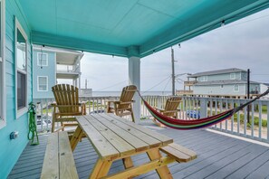A wooden deck with picnic tables and chairs, a hammock, and a view of the ocean and other buildings. - Furnished Deck + Ocean Views: Surfside Beach Home (Freeport)