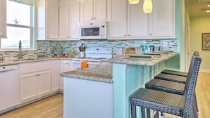 A kitchen with white cabinets, a microwave, a stove, and a sink. There is a window with a view of a hill. - Furnished Deck + Ocean Views: Surfside Beach Home (Freeport)
