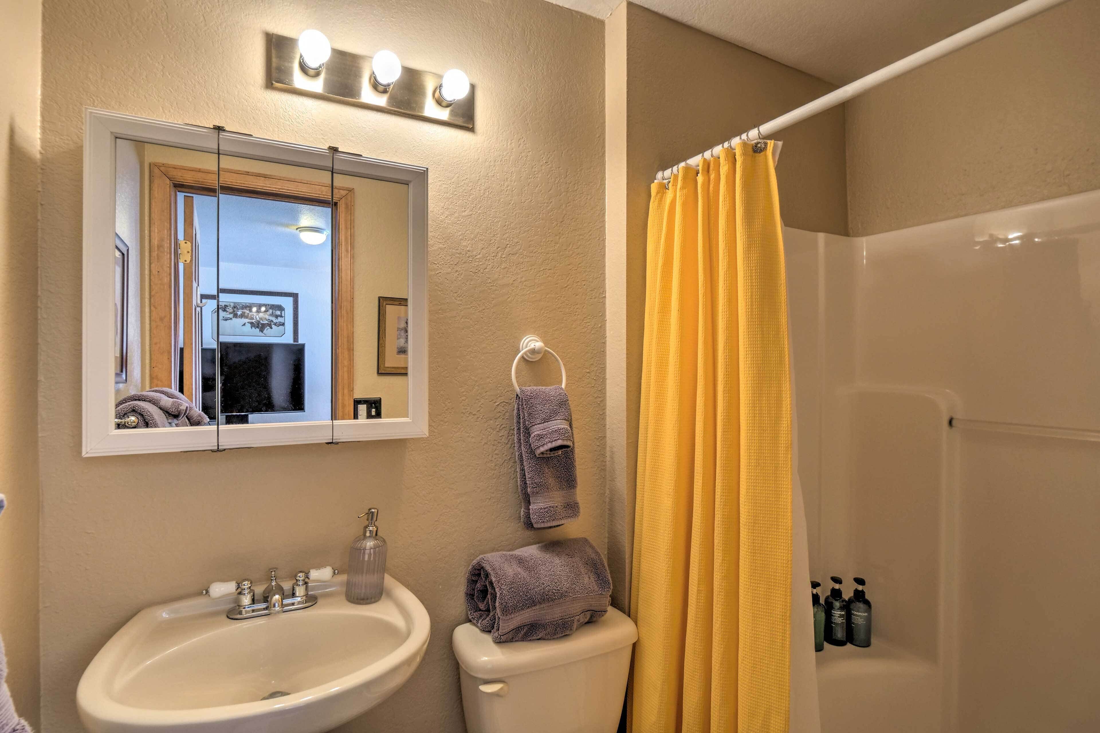 A bathroom with a sink, mirror, and toilet. There are towels hanging on the wall and a shower curtain.