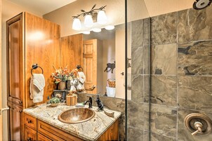 Un baño con tocador de madera, un espejo grande, un lavabo y una zona de ducha con baldosas de piedra.
