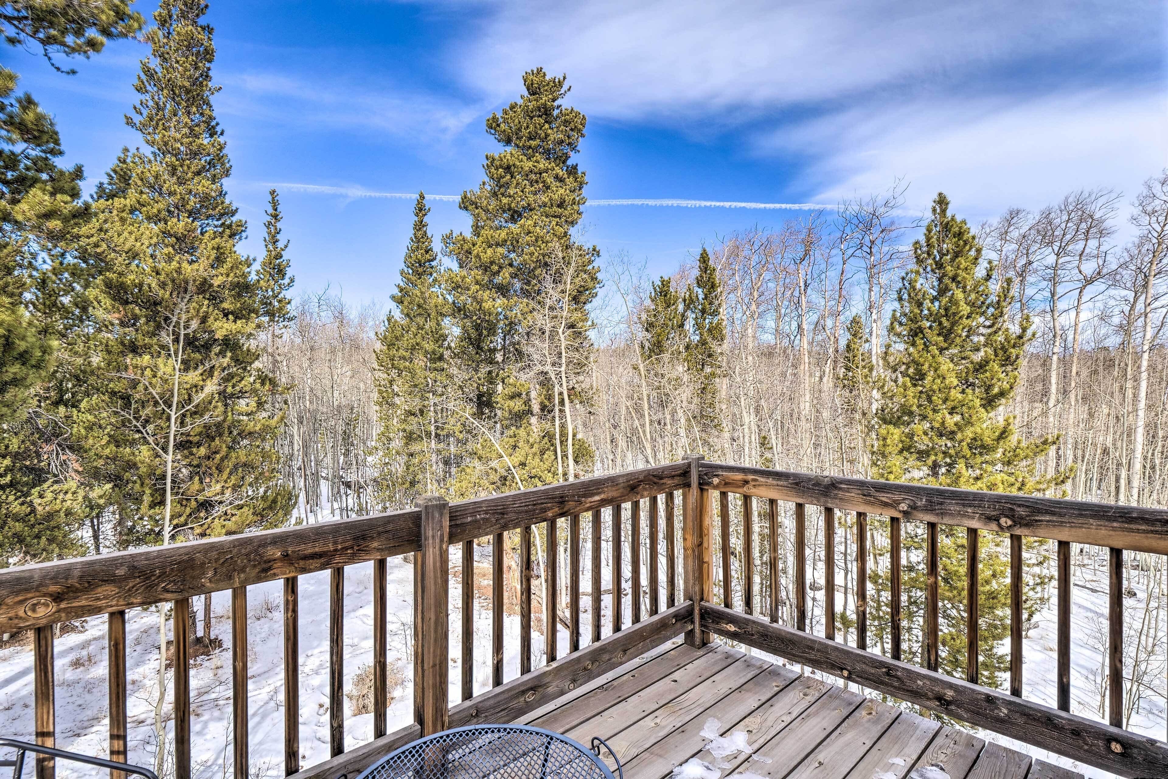 A wooden deck with a metal chair, surrounded by trees and snow.
