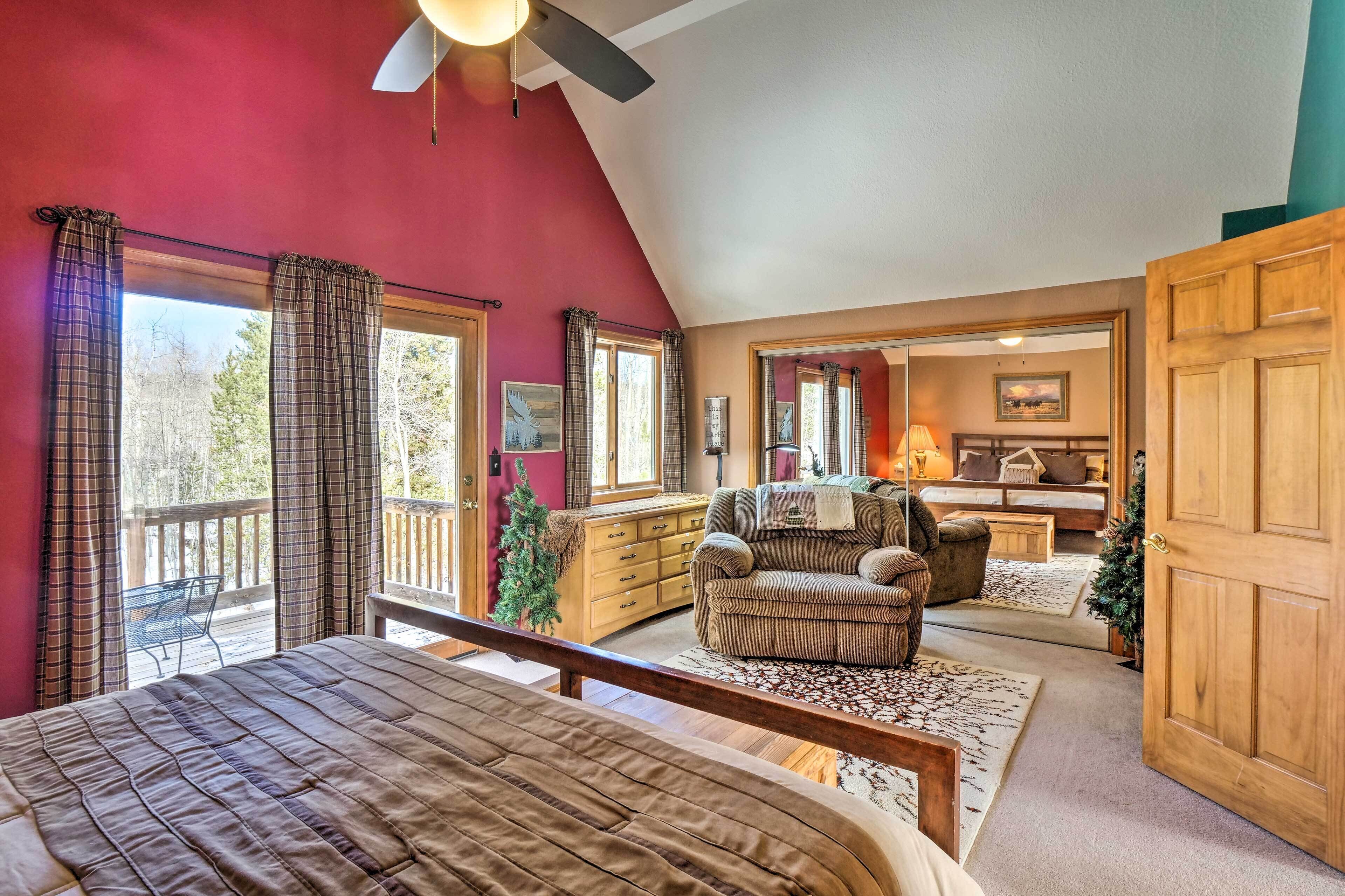A bedroom with a large bed, a wooden desk, a chair, and a balcony with a view of trees.